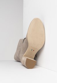 Beige Wildleder-Ankle-Boot mit durch perforiertes Design, leicht geschwungener Ferse und Gummisohle. Verfügt über prägierte Markenlogo und Größenangaben.