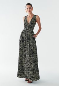 Vestido largo de tela negra con un estampado de hojas en dorado. Presenta un escote en V profundo, cintura entallada y bolsillos laterales. Textura suave.