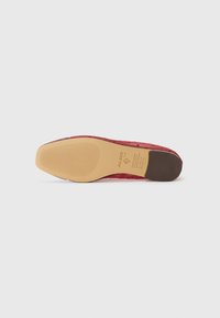 Pink textured shoe sole with rubberized brown heel, featuring a patterned grip and embossed brand logo on the bottom.