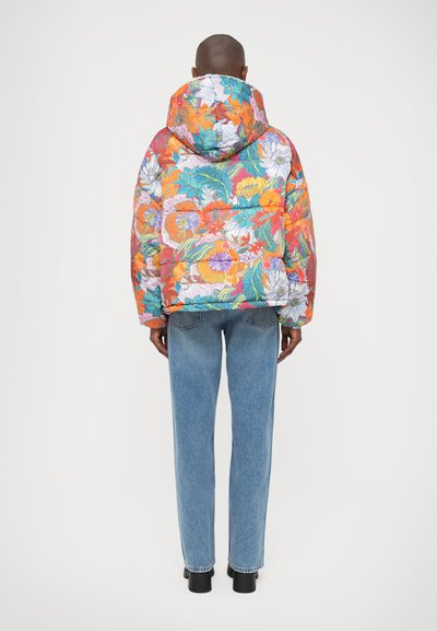 Farverig blomsterpufjakke med hætte; har en række lyse mønstre på en quiltet overflade, parret med lyseblå jeans.