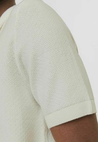 Polo shirt a maniche corte in maglia di un beige chiaro, caratterizzato da un tessuto texture e colletto e polsini a costine. Il design senza cuciture aumenta il comfort.
