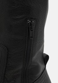 Musta nahkasaapas, jossa on sivuvetoketju ja hillitty teksturoitu pinta. Saapas sisältää pehmustetun yksityiskohdan nilkan lähellä mukavuutta varten.