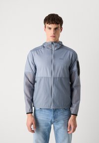 Lightweight gray hooded jacket with a zip front, elastic cuffs, and a sleek design. Features a distinctive black logo on the left arm.