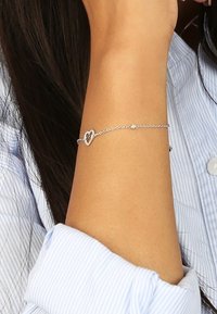 Zilveren kettingarmband met een hartvormige bedel, met een delicate ontwerp en kleine accentparels, gedragen om een pols.