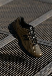 Brown and black athletic shoe with a textured upper, lace-up closure, and padded collar, set against a grid pattern background.