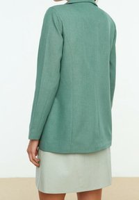 Blazer en lin vert, coupe ajustée, manches longues et col cranté, associé à une jupe en cuir gris clair. Texture lisse.