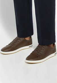 Brown leather sneakers featuring a textured woven pattern, round toe, lace-up design, and white rubber sole with subtle color accents.
