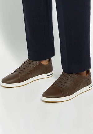 Brown leather sneakers featuring a textured woven pattern, round toe, lace-up design, and white rubber sole with subtle color accents.