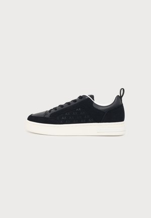 Zwarte lage sneaker met witte zool, veters aan de voorkant, trek-lus aan de hiel en een subtiel "AX" patroon op het zijpaneel.