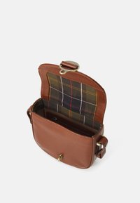 Hnědá kožená taška přes rameno s klopovým uzávěrem; interiér má podšívku z kostkované látky ve tmavě zelené, žluté a červené barvě.