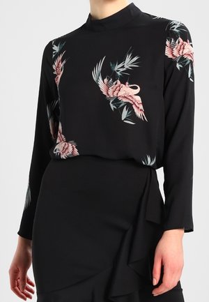 Sort langærmet top med pink trane og grønne blade, kombineret med en sort højtaljet nederdel med en flæsedetalje i siden.