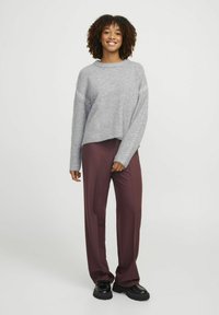 Pull gris court avec des manches texturées. Associé à un pantalon large bordeaux et des chaussures noires épaisses. Fond neutre.