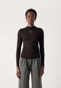 Black long-sleeve top with a fitted, textured design and subtle ruching. Features a small DKNY logo at the chest. Paired with gray trousers.