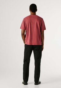 T-shirt met korte mouwen en een ronde hals in vervaald bordeauxrood, gecombineerd met een zwarte broek, met een losse pasvorm en subtiele stiksel details.