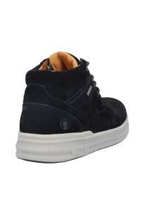 Zapato negro de ante de caña media con un forro interior marrón claro, cordones robustos y suela de goma blanca. Presenta un logo en el lado exterior.
