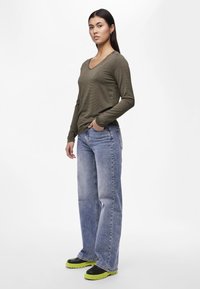 Olivengrønn langermet V-hals topp, lyseblå høyt liv jeans, og svarte sko med grønne såler. Jevn tekstur og avslappet passform.