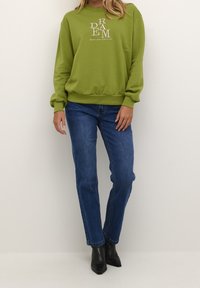 Groene katoenen sweatshirt met witte "DREAM" tekst, geribbelde manchetten en zoom. Gecombineerd met donkerblauwe jeans met rechte pijpen en zwarte enkellaarsjes.