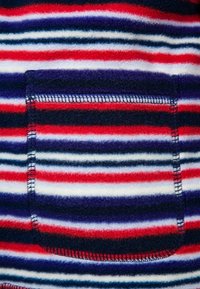 Fleecová látka s vodorovnými pruhy v červené, námořnické, fialové a bílé; obsahuje náprsní kapsu a viditelné švy.