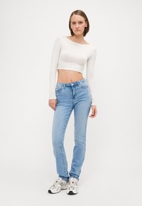 Fehér, hosszú ujjú cropped top, világoskék, egyenes szárú farmernadrággal párosítva. A tornacipők fehér és szürke színkeverékkel rendelkeznek, fekete részletekkel.