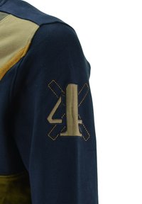 Giacca in pile navy e khaki con un grande "4" ricamato e un accento di linee incrociate sulla spalla sinistra. Texture morbida, design casual.