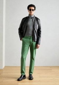 Sort læderjakke, grå turtleneck, grønne bukser og sorte sko. Glatte teksturer og skræddersyet pasform med minimalistiske designelementer.