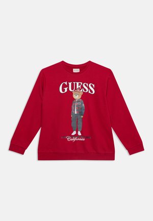 Κόκκινο φούτερ μακρυμάνικο με κείμενο "GUESS" και μια αρκούδα που φοράει μπουφάν και καπέλο τυπωμένη μπροστά, με "California" από κάτω.