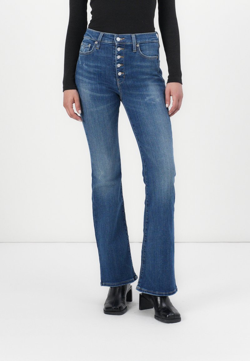 Jeans a vita alta in denim blu, a gamba svasata, con patta a bottone, cinque tasche e leggere scoloriture. Indossati con stivali neri con tacco.