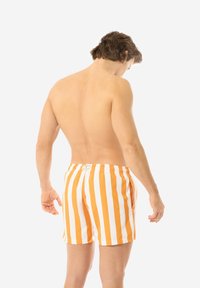 Orange und weiße gestreifte Badehose aus leichtem Material, mit elastischem Bund und Seitentaschen, von hinten betrachtet.