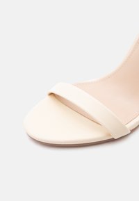 Κοντινό πλάνο μπεζ σανδάλι με ανοιχτές μύτες, μία μπροστινή λωρίδα και λείο πέλμα σε λευκό φόντο.
