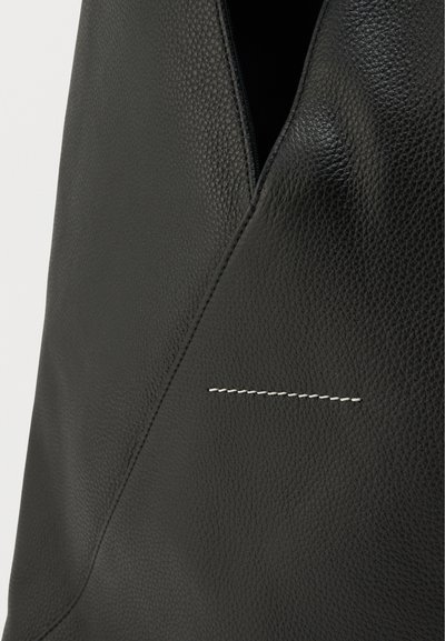 Črna usnjena torba s teksturirano površino in značilnim všitim detajlom. Dizajn vključuje edinstven diagonalni rez na vrhu.