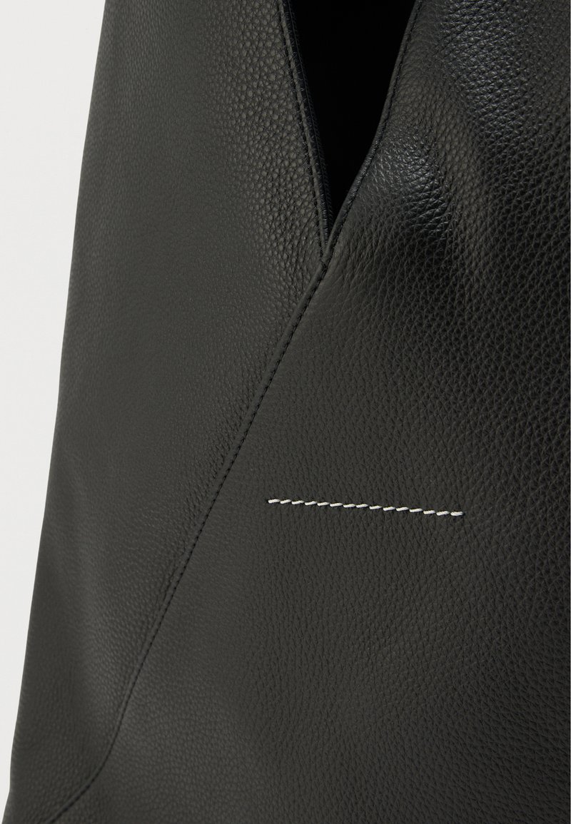 Sort lædertaske med en struktureret finish og et karakteristisk syningsdetalje. Designet inkluderer et unikt diagonalt snit øverst.