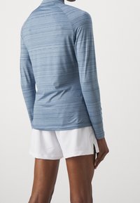 Long-sleeve athletic top in light blue with horizontal stripes, featuring a high neckline and a fitted design. Paired with white shorts.