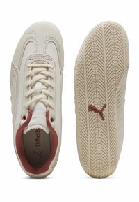 Zapatillas deportivas con parte superior de cuero color crema y acentos rojos, con un sistema de cordones en la parte delantera y una suela de goma texturizada con patrón de tracción. Detalle de plantilla Ortholite.
