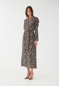 Blommönstrad långärmad klänning i beige och marinblå. Har en V-ringning, rynkade puffärmar och ett knytbälte i midjan. Slät tyg.