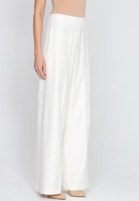 Białe szerokie spodnie z gładką teksturą, wysokim stanem i pionowymi szwami. W połączeniu z cielistymi butami na szpilkach.