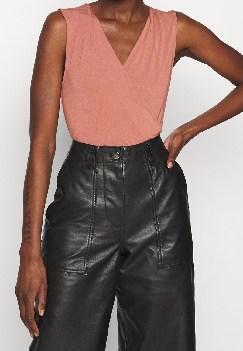 V-neck, short-sleeve top in dusty rose fabric, paired with high-waisted black leather trousers featuring front pockets and visible seams.