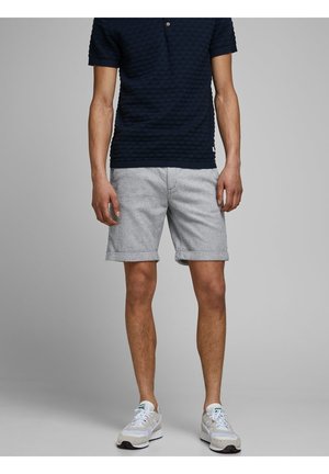 Granatowa polo z fakturą, z krótkim rękawem, zestawiona z jasnoszarymi, casualowymi szortami. Model ma na sobie białe sneakersy z akcentami.