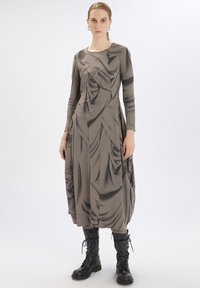 Vestido de manga larga hasta la rodilla en beige con textura drapeada. Combinado con botas de combate negras con cordones. Material suave y elástico con detalles.