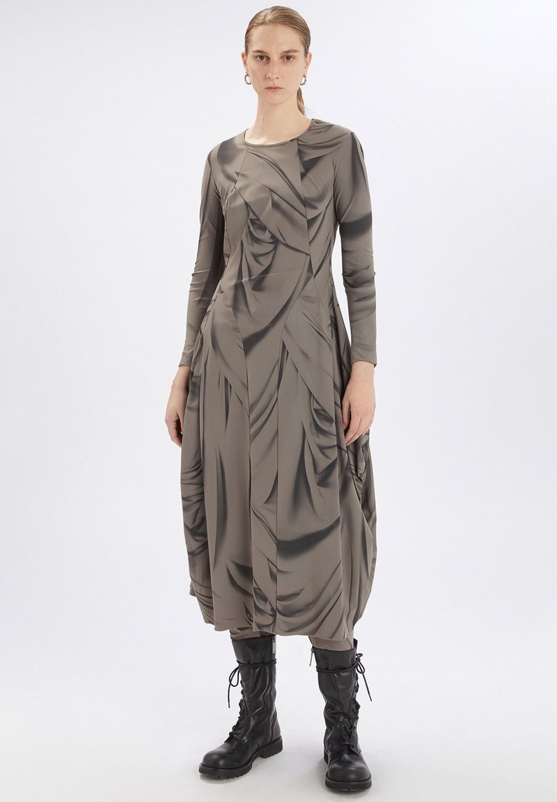 Vestido de manga larga hasta la rodilla en beige con textura drapeada. Combinado con botas de combate negras con cordones. Material suave y elástico con detalles.
