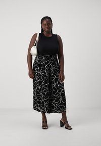 Black sleeveless top paired with black and white patterned wide-leg pants. The outfit is complemented by a small white handbag and block-heeled sandals.