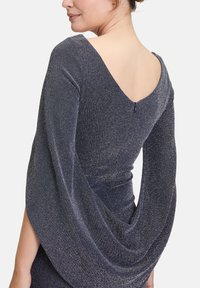 Robe bleu marine avec un dos en V, des manches longues et des détails drapés. Fabriquée dans un tissu texturé et scintillant avec un éclat subtil. Fermeture éclair au dos.