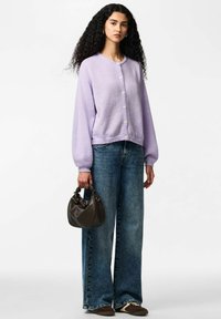 Lavendelgekleurde gebreide cardigan met een ronde hals en knoopsluiting, gecombineerd met wijduitlopende blauwe spijkerbroek en een kleine donkere handtas.