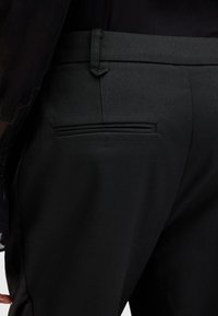 Svarta skräddarsydda byxor med en mjuk textur, med en bakficka med en smal horisontell öppning och en åtsittande midja.