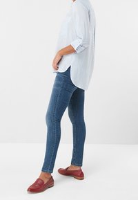 Camicia button-up a strisce bianco e azzurro, jeans in denim blu aderenti e mocassini borgogna con dettagli a borchie. Panoramica sull'outfit casual.