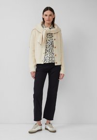 Cardigan en maille crème avec fermeture à boutons, associé à une chemise à imprimé léopard noir et blanc, un pantalon noir et des baskets beiges avec des accents blancs.