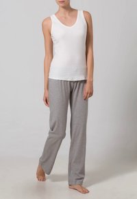 Balta bezpiedurkņu V veida kakla blūze apvienota ar pelēkajām brīvā griezuma biksēm. Abiem apģērbiem ir mīksta auduma struktūra ar gludu tekstūru.