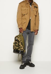 Plecak kamuflażowy z detalem z teksturowanej tkaniny, w kolorach oliwkowej zieleni i czerni, o zaokrąglonym kształcie i spodzie z syntetycznej skóry.