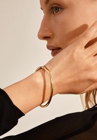 Bracelet en or exposé sur une main. Le bracelet est élégant et lisse, avec un design rond simple et une finition polie.