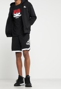 Svart Adidas zip-up hoodie, svart grafisk t-shirt med röda detaljer, svarta shorts med vit kant, och svarta sportskor.