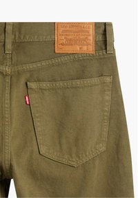 Vaqueros de mezclilla verde oliva con un bolsillo trasero que tiene la etiqueta roja de Levi's y un parche de cuero marrón de la marca Levi Strauss & Co. en la cintura.